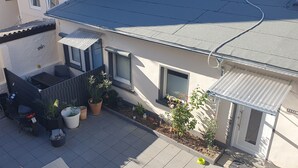 Een woongebouw met een betegeld terras, een scooter, potplanten en een kleine tuin.