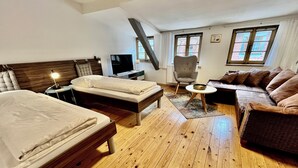 A hotel room with two beds, a sofa, a chair, a TV, and a window. - live individually and modernly in old walls (Görlitz)