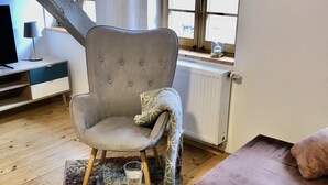 A cozy living room with a grey armchair, a round coffee table with a book and glasses, a brown sofa, and a window with curtains. - live individually and modernly in old walls (Görlitz)