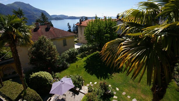 A garden with a patio, a view of a lake, and a mountain in the background. - Rustic modern apartment with atmosphere at Lago Maggiore (Verbania-Biganzolo)