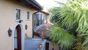 A building with a tiled roof, a stone archway, and a small balcony with a potted plant and a vase. - Rustic modern apartment with atmosphere at Lago Maggiore (Verbania-Biganzolo)
