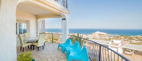A balcony with a view of the sea, a dining area with chairs, and a potted plant.