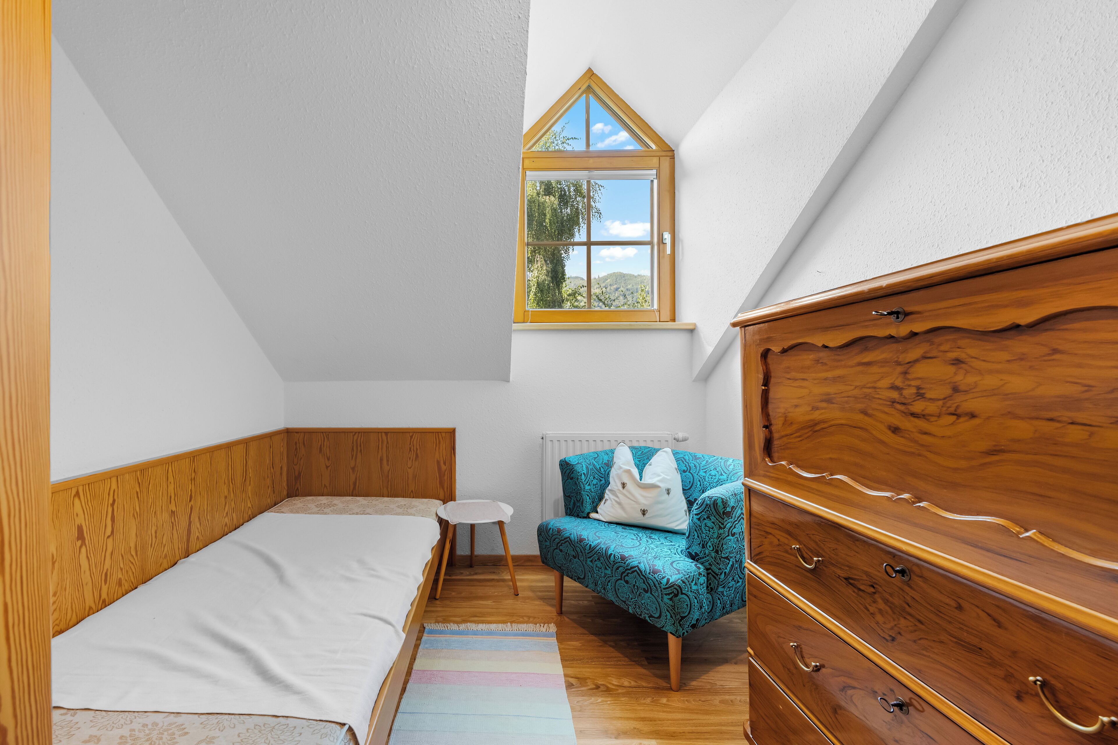 Una camera da letto con un letto, una cassettiera, una sedia, un tavolino e una finestra vista all'esterno.