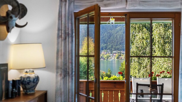 Une pièce avec vue sur un lac et une forêt, une table en bois et une lampe sur une table d’appoint.