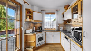 Une cuisine moderne avec des meubles en bois, un four encastré, un four à micro-ondes et une grande fenêtre donnant sur un paysage verdoyant.