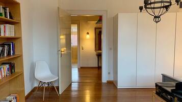 A modern living room with a wooden floor, a white chair, a bookshelf, a small rug, and a suitcase.
