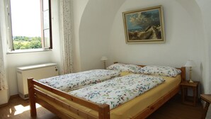 Une chambre avec deux lits simples, une fenêtre avec des rideaux, un radiateur, un tableau au mur et une table de chevet avec une lampe.