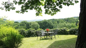Une terrasse avec une table et des chaises, entourée d’une végétation luxuriante et d’arbres.