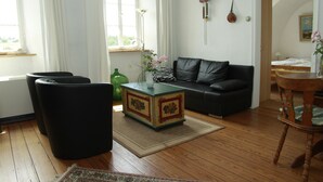 Un salon avec un canapé noir, une table basse en bois et un vase vert contenant des fleurs.