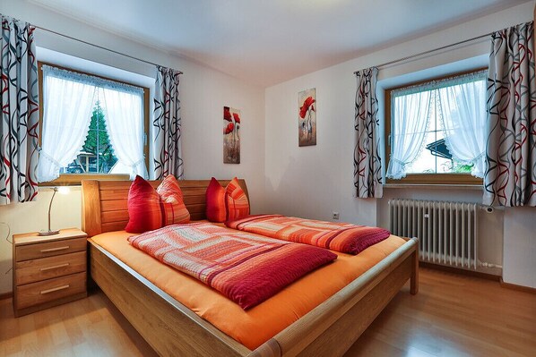 Un dormitorio con cama de madera, dos ventanas con cortinas, un radiador y obras de arte en las paredes.