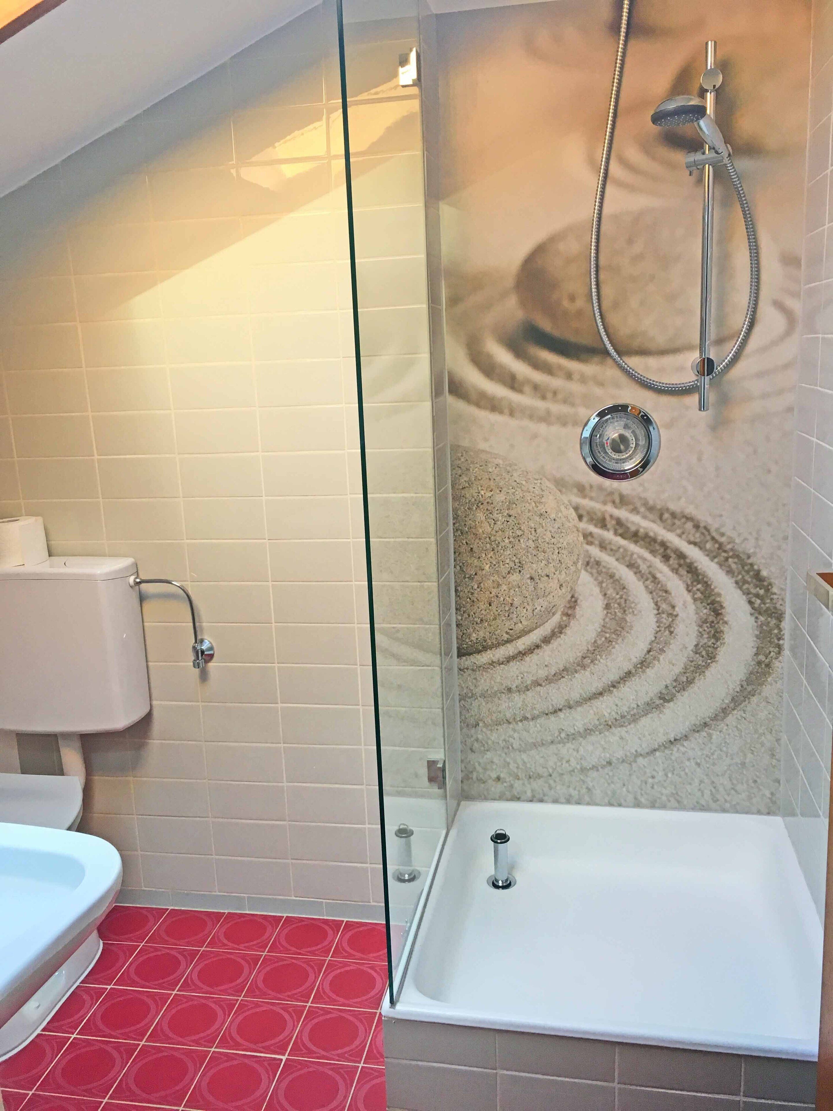 Une salle de bain avec une douche à parois de verre, des toilettes blanches et un sol à motifs rouges.