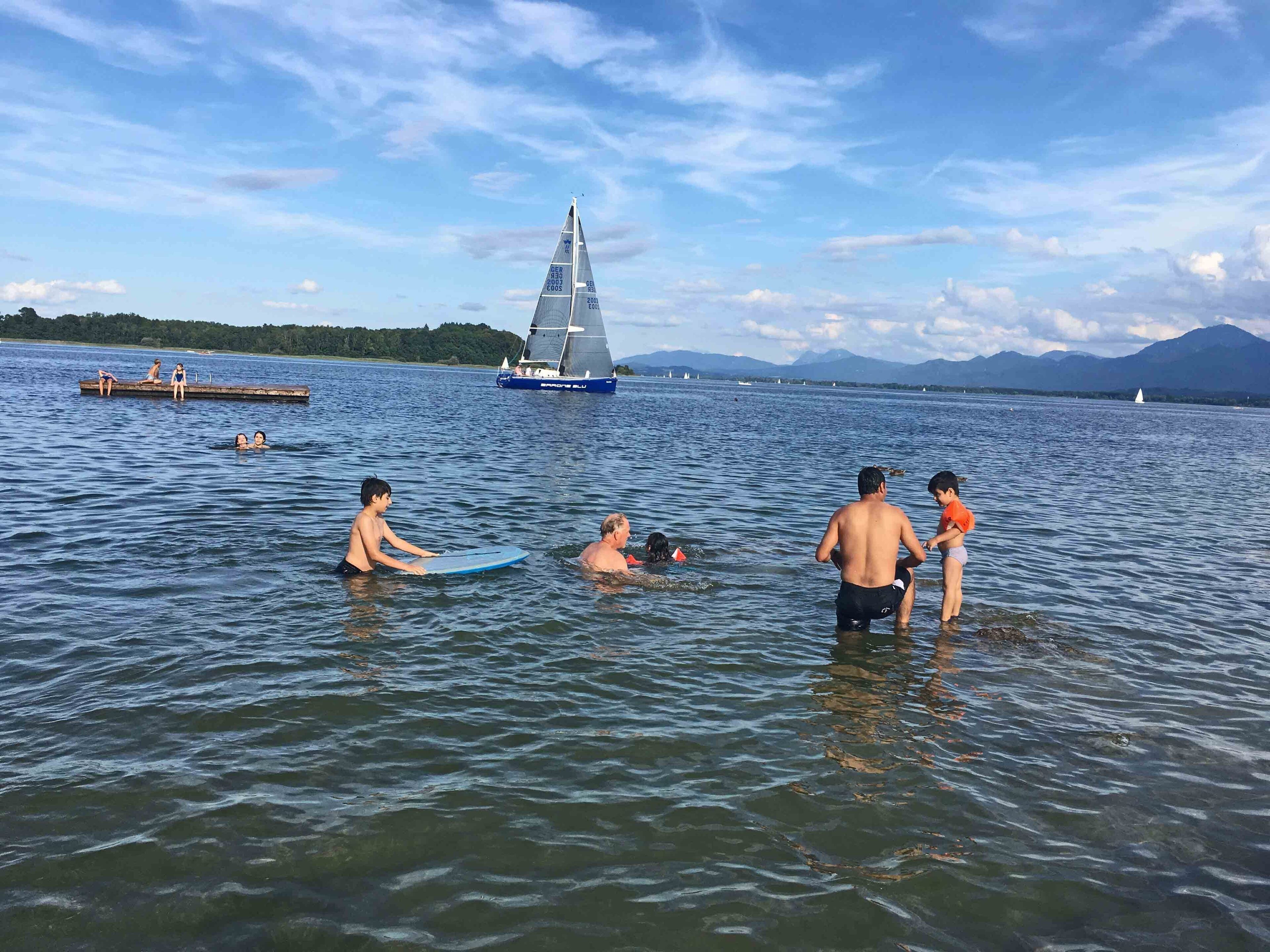 Un lac où des gens se baignent et où l’on aperçoit un voilier au loin.