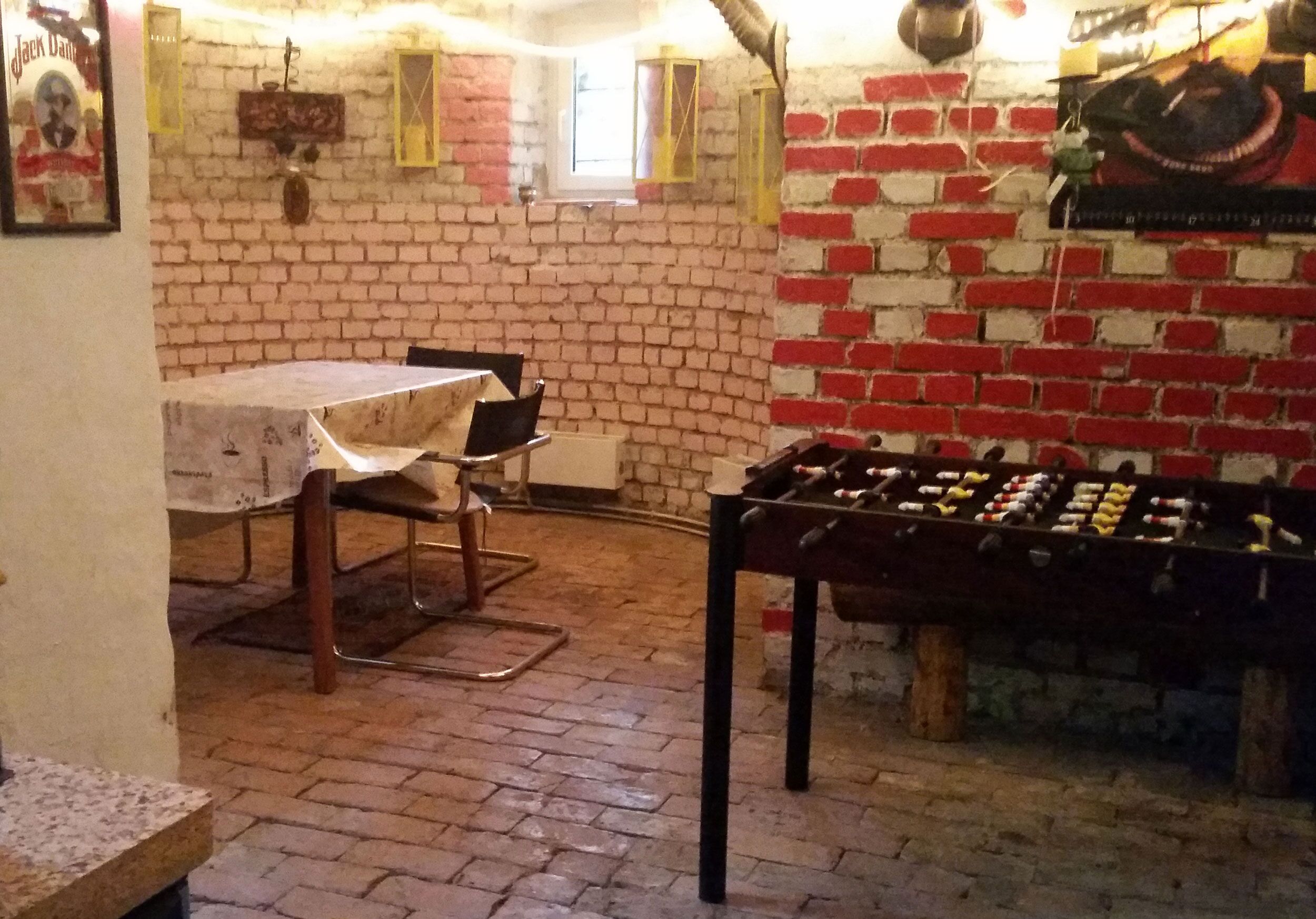 Una habitación con pared de ladrillo, mesa de fútbolín, mesa con sillas y una ventana.