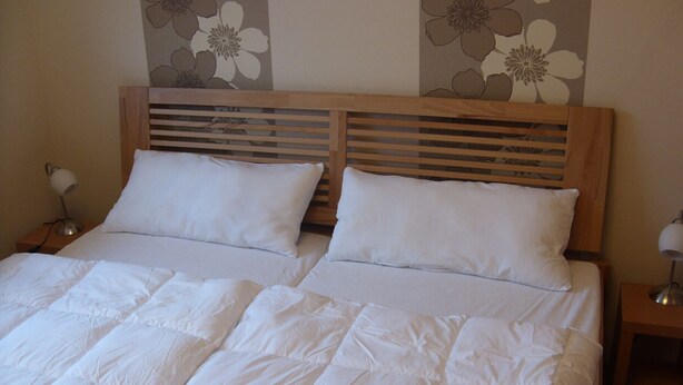 A double bed with white bedding, two pillows, and a wooden headboard with horizontal slats. - Nice apartment near the beach and the center (Grömitz)