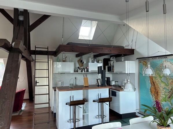 A modern kitchen with white cabinets, a wooden island with bar stools, a map on the wall, and a skylight. - Attic studio in the Geteviertel - close to the city, trade fair, university, stadium and Weser cycle path (Schwachhausen)
