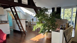 A spacious living area with a large potted plant, wooden flooring, and a loft space above. - Attic studio in the Geteviertel - close to the city, trade fair, university, stadium and Weser cycle path (Schwachhausen)