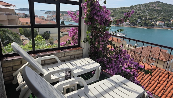 A balcony with white chairs and a table, overlooking a coastal town with boats and buildings. - Luxury apartment with panoramic sea view in Tisno, only 100 steps to the sea (Tisno)