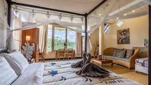 A bedroom with a canopy bed, a sofa, a dining area, and a painting on the wall. - Tirta Asri Ubud Villa (Ubud)