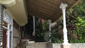 A covered outdoor area with a tiled staircase leading to a higher level, surrounded by greenery and a white column. - Tirta Asri Ubud Villa (Ubud)