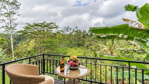 A balcony with wicker furniture, a table with a fruit bowl, a bottle, and a glass. - Tirta Asri Ubud Villa (Ubud)