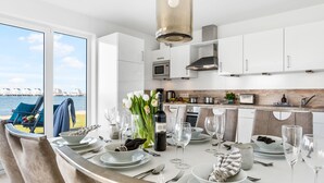 Una cucina moderna con mobili bianchi, un tavolo da pranzo apparecchiato per sei e vista mare attraverso ampie finestre.