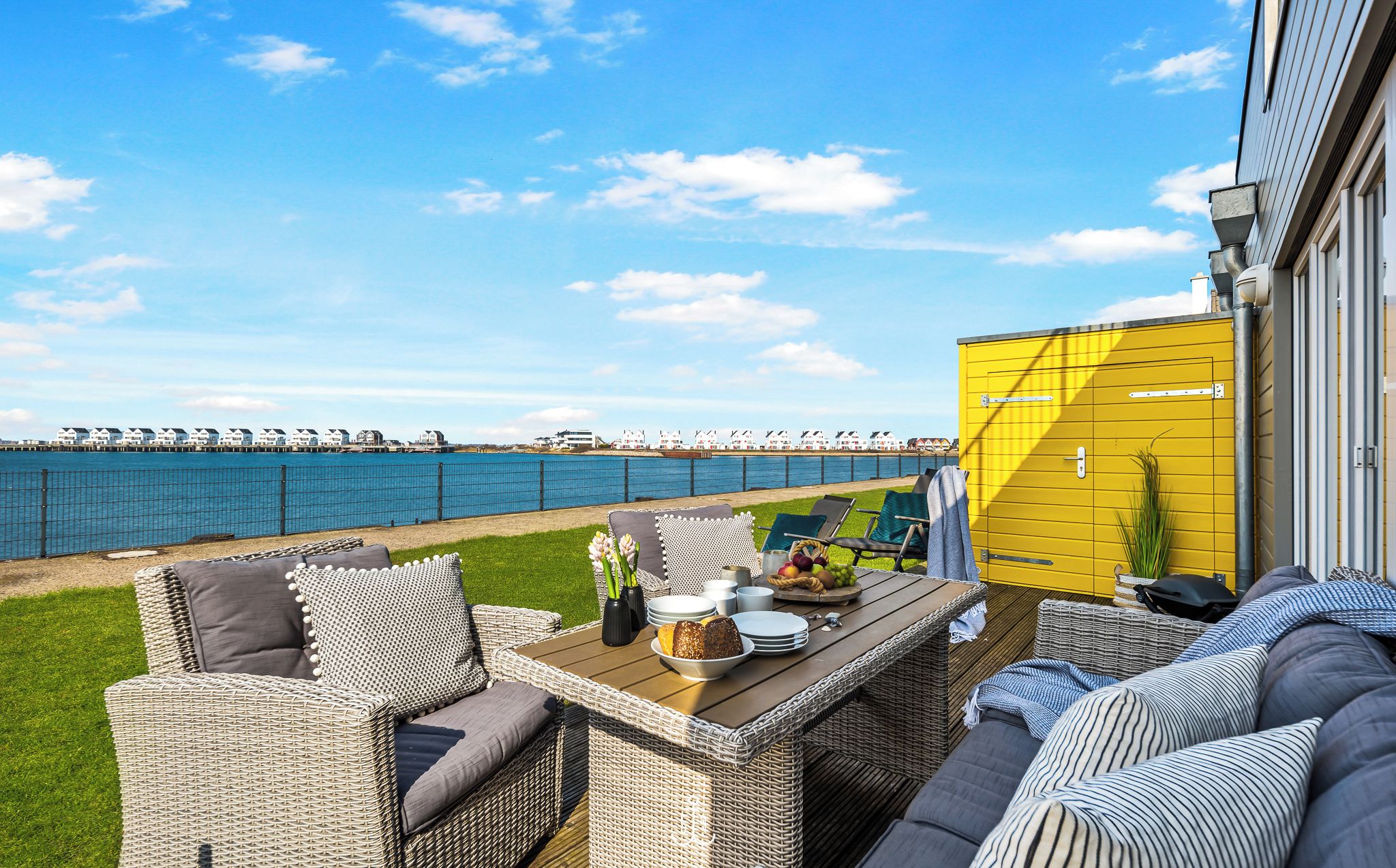Une terrasse dotée de meubles en osier, d’une table à manger et d’un bâtiment jaune.