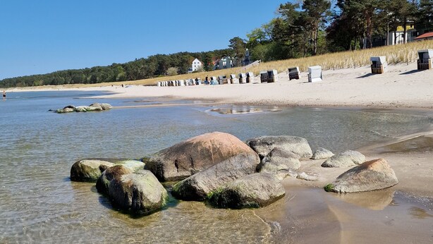 En strand med klart vand, store sten og en sandet kyst.