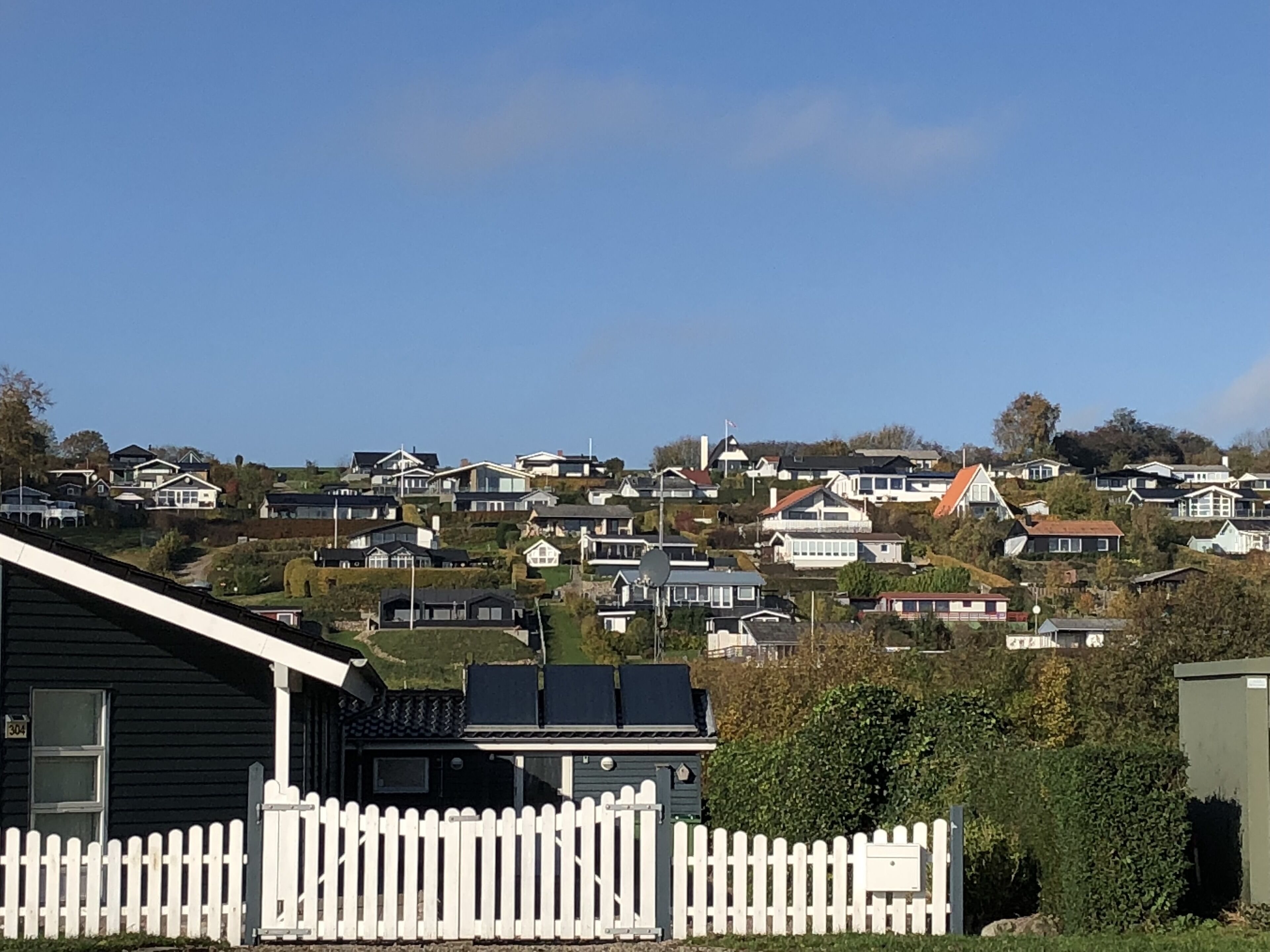 A residential area with houses on a hillside, a white picket fence, and a clear blue sky.