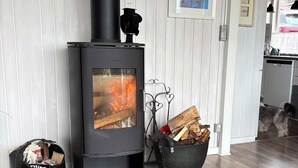 Une pièce moderne équipée d’un poêle à bois, d’une cheminée, où un chien se trouve, et comprenant un coin repas.