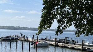 Un port de plaisance avec des bateaux amarrés, une jetée s’avançant dans une eau calme, et une branche d’arbre encadrant partiellement le paysage.
