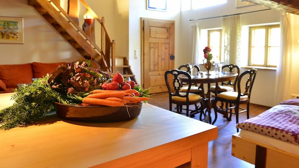 A dining area with a wooden table, chairs, and a bowl of vegetables.