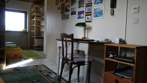 Ein Zimmer mit Schreibtisch, Stuhl, Lampe, Bücherregal und Heizkörper.