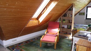 Ein gemütliches Schlafzimmer im Dachgeschoss mit schrägen Wänden, einem roten Sessel, einem Bücherregal und einem Schreibtisch mit einem Laptop.