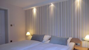 Una habitación de hotel con una cama grande, dos mesitas de noche con lámparas y un muro a rayas.