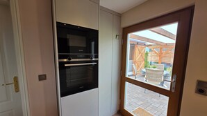Una cocina con horno Siemens, un armario blanco y una puerta de madera que da a un área exterior con patio.