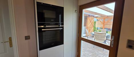 A kitchen with a Siemens oven, a white cabinet, and a wooden door leading to an outdoor area with a patio.