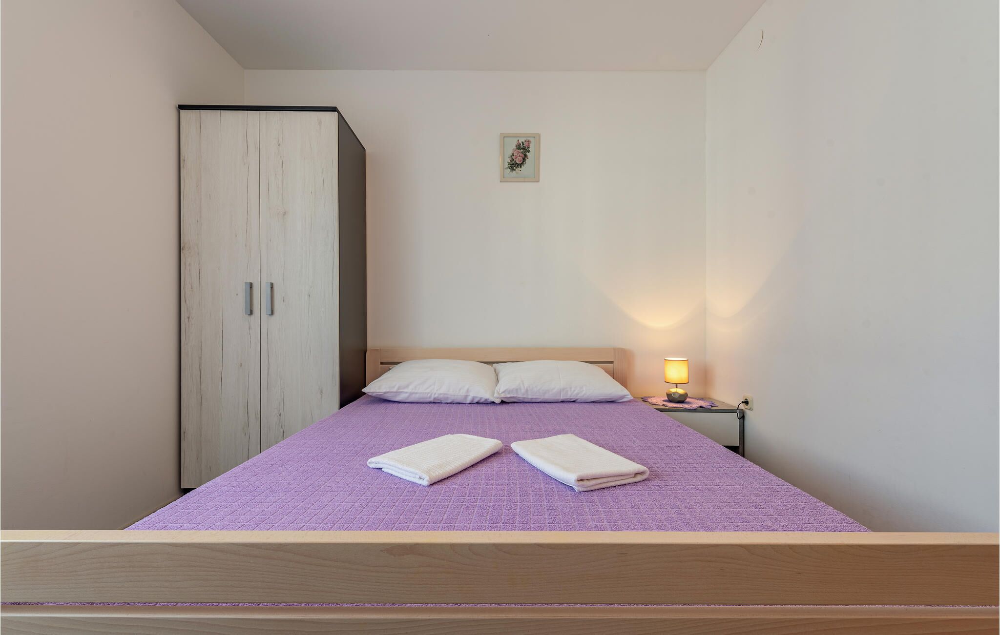 A single bed with a wooden headboard, a nightstand with a lamp, and a wardrobe with two doors.