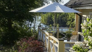 A wooden deck with a white umbrella, a chair, and a potted plant. - Idyllic lakeside location, luxury furnishings - sauna, boat, canoe, WLAN, 3 bedrooms. (Nybro S)
