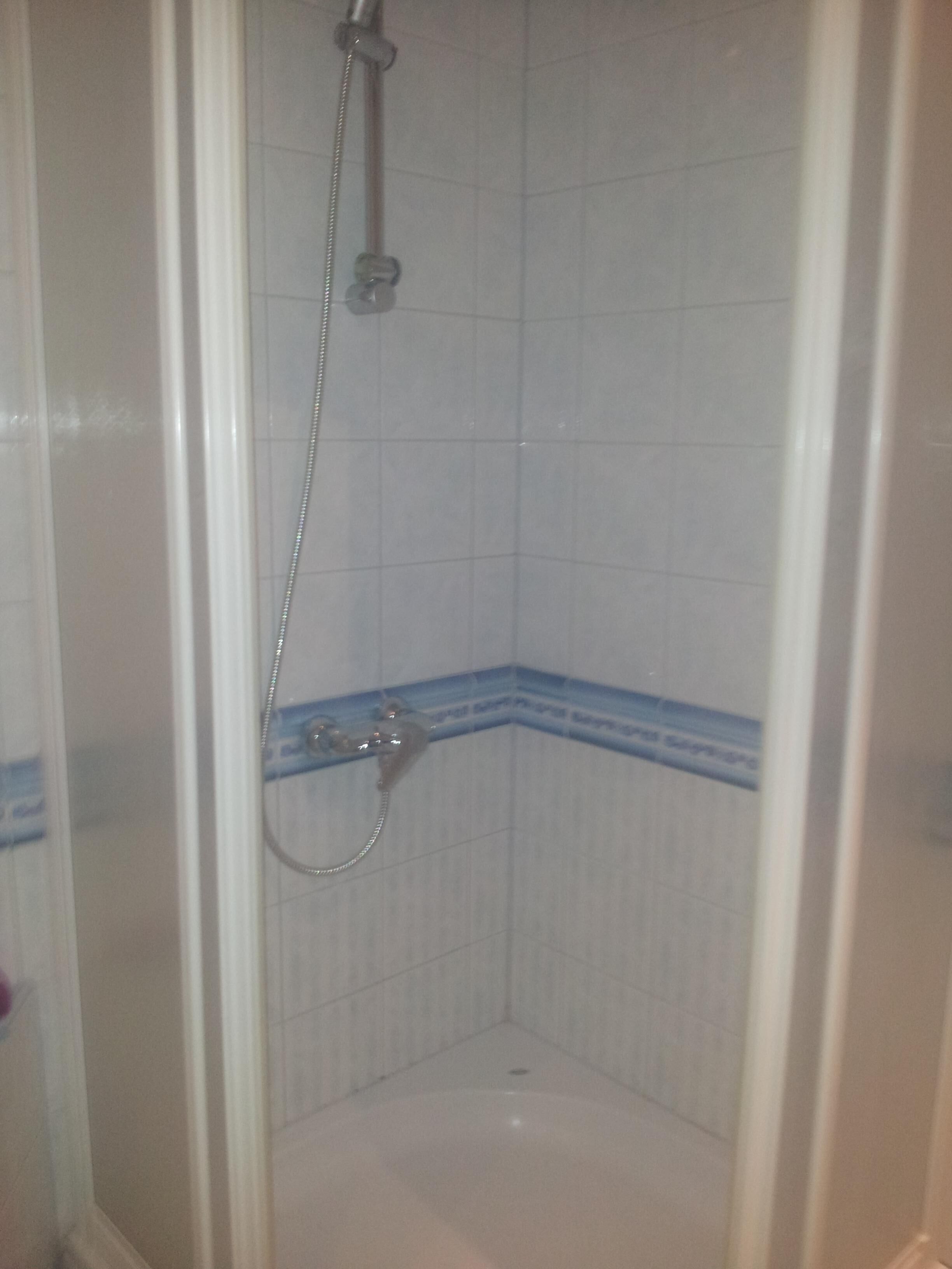 Un espacio de ducha pequeño y cerrado, con azulejos blancos y detalles azules.