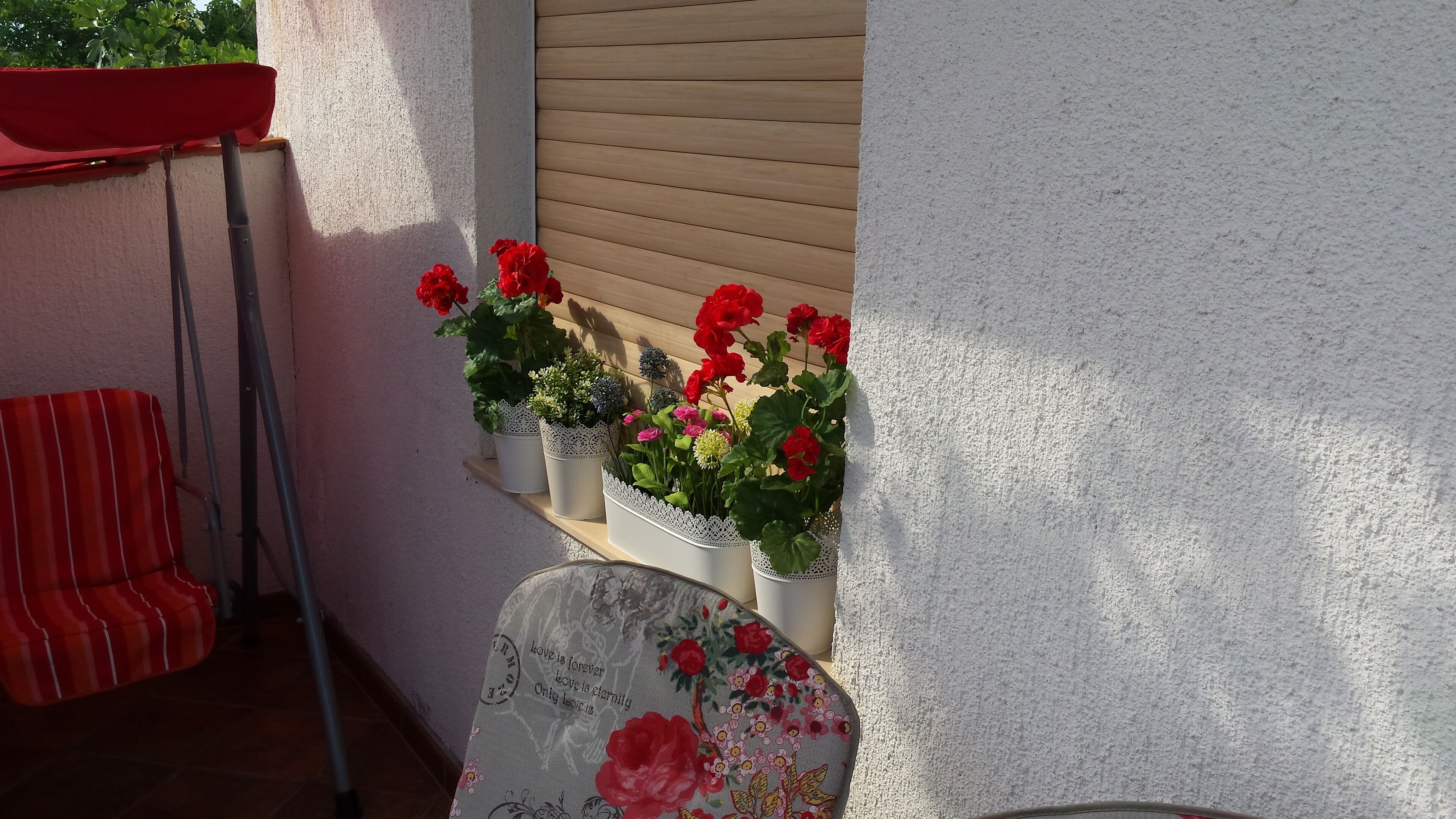 Un balcón con plantas en macetas y una silla roja.