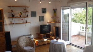 Un salon chaleureux avec un téléviseur, des étagères en bois et un fauteuil en osier.