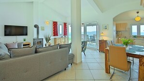 A spacious living area with a sofa, TV, and a fireplace. There is a dining area with a table and chairs, and a kitchen visible through an open doorway. - Holiday house with fantastic sea view and pool - spring offer from 27. 4.-19. 5th (Ripenda Kosi)