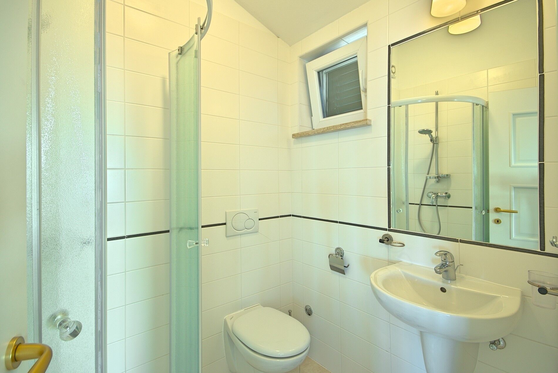 Et badeværelse med toilet, håndvask og brusekabine i glas.