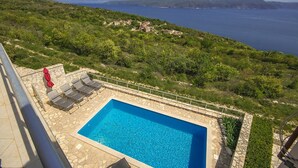 A swimming pool with a stone border, surrounded by a stone deck, overlooking a coastal landscape with hills and a clear blue sea. - Holiday house with fantastic sea view and pool - spring offer from 27. 4.-19. 5th (Ripenda Kosi)