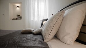 A neatly made bed with a quilted cover and patterned pillows, a bedside table with a vase of flowers, and a wall-mounted light fixture.
