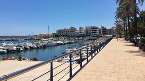 A marina with boats docked, a paved walkway, and buildings in the background.