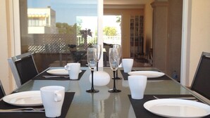 A dining table set with white plates, cups, and wine glasses, with chairs around it.