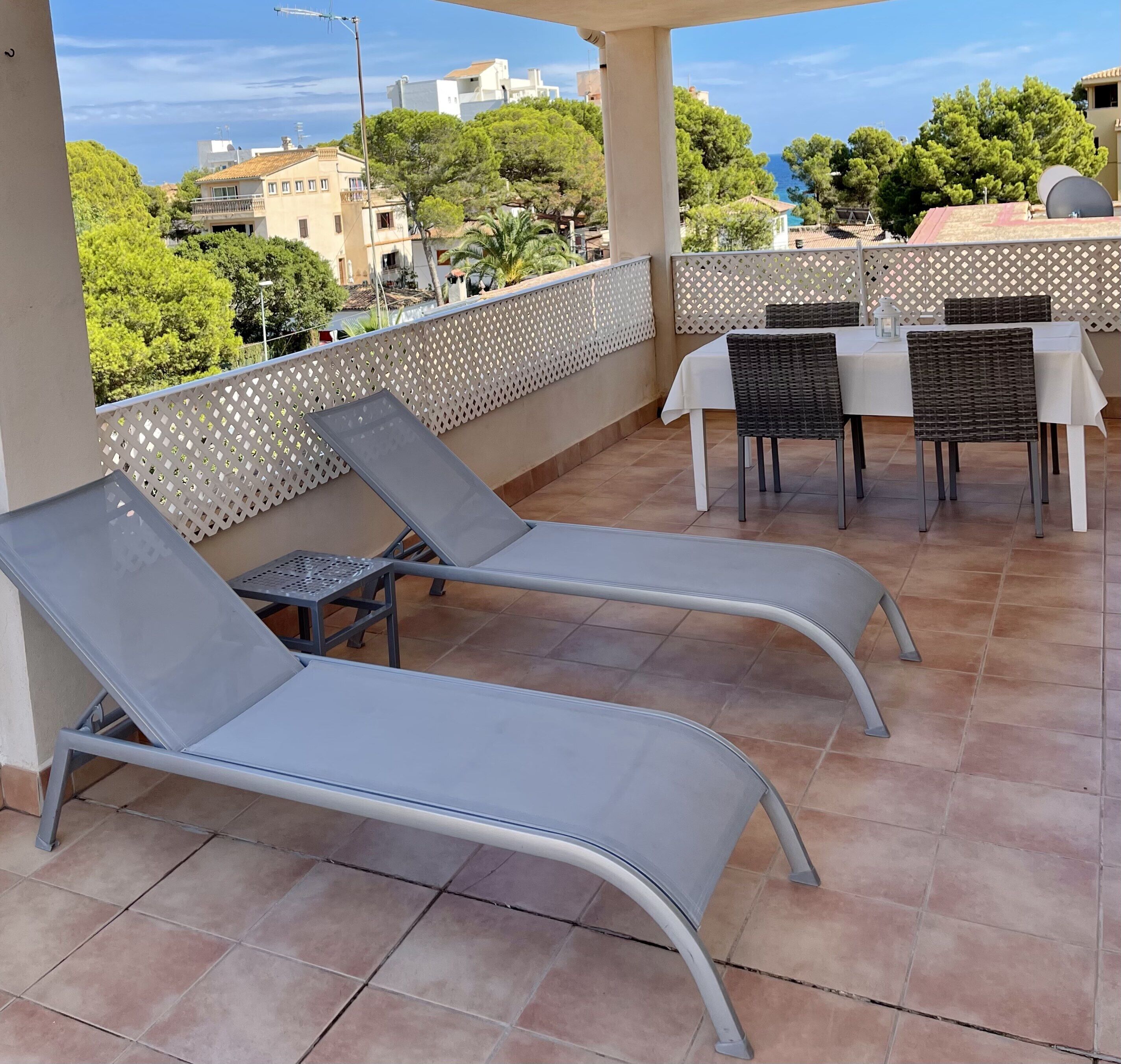 A terrace with two lounge chairs, a table, and chairs, overlooking a residential area with trees and buildings.