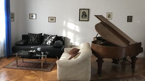 Un salon avec un canapé noir, un fauteuil blanc, une table basse en verre et un piano à queue.