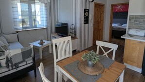 Ein gemütliches Wohnzimmer mit Sofa, einem Esstisch mit Stühlen, einem Fernseher und einer Küchenzeile mit Mikrowelle.
